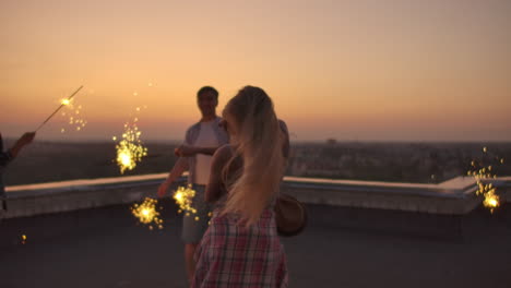 Russian-blonde-on-the-roof-moves-her-arms-and-body-beautifully-a-dance-with-her-friends-on-a-summer-evening-with-big-bengal-light.-Her-hair-blows-beautifully-in-the-wind.